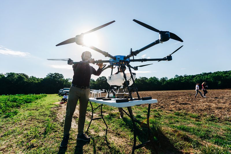 person working on a large drone, crop fields, sunshine