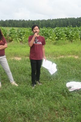 A young man with a microphone speaks in the field.