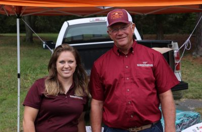 A woman and man wearing Virginia Tech shirts greet visitors at the entrance to Family & Farm Day.