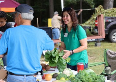 A woman holding a cabbage talks with Family & Farm Day guests at a booth set up with vegetables.