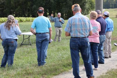 A VCE agent holding a microphone speaks to a group during field day.