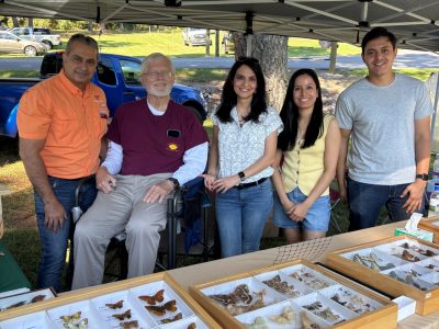 Five people smile from behind a table with insect specimens