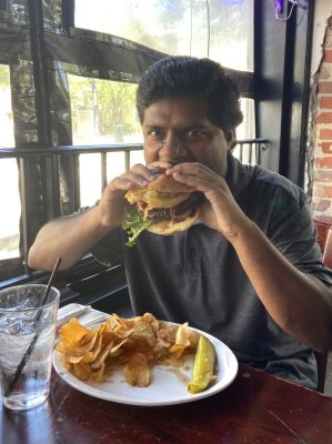 man in gray polo shirt eats burger and chips at restaurant.