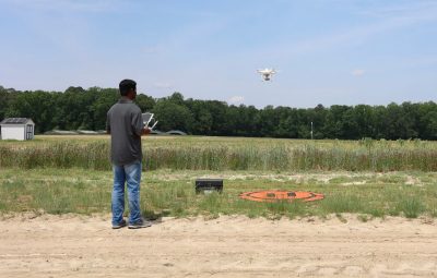 man in gray shirt and jeans flies drone over farm field.